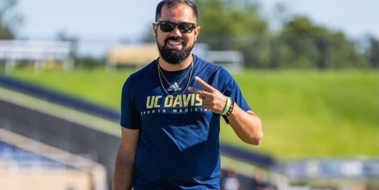Photo shows Kyle Schank walking on a sports field and smiling. 