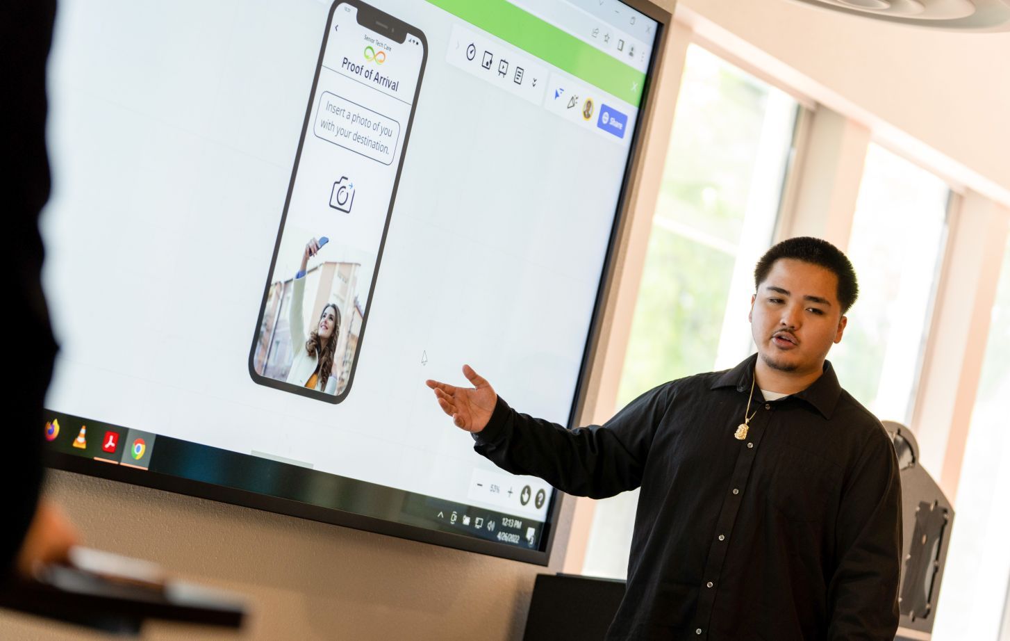 A student stands next to a projection screen with an app displayed
