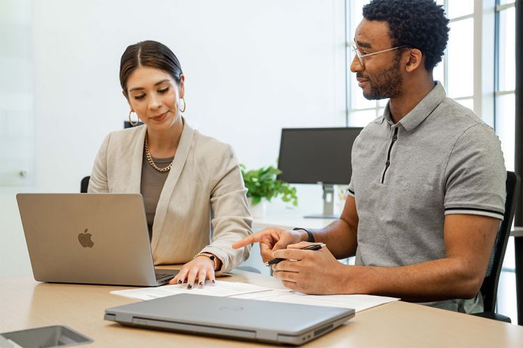 Two people sit at a table looking at a computer