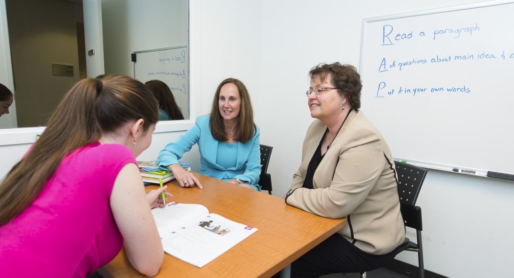 Image shows two Speech-Language Pathology faculty members sitting across a table from a student. 