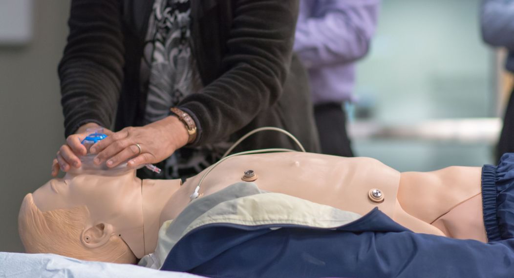 Photo shows a student standing next to a manikin while practicing putting on a breathing mask. 