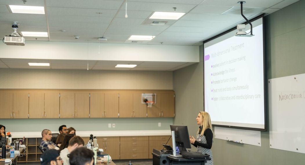 Photo shows a lecturer speaking in front of a class in the CPAE classroom.