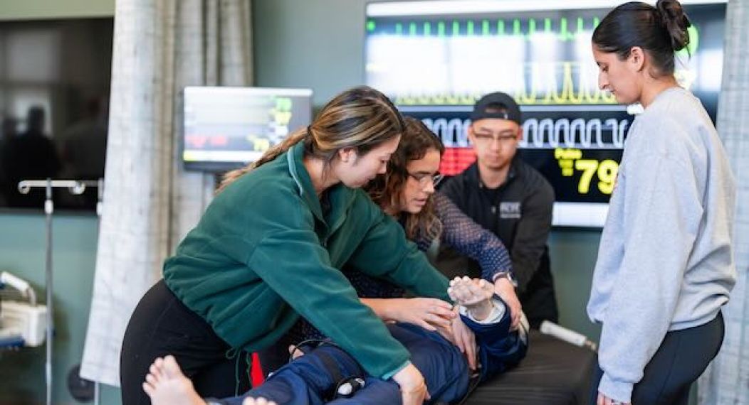 Image shows three students being instructed on a procedure on a mannequin