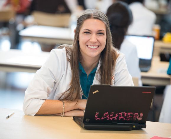 student in white coat in front of laptop