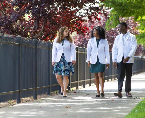 students in white coats walking on sidewalk