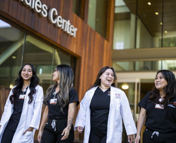 Photos shows four nursing students from Pacific's School of Health Sciences smiling as they walk near the nursing classroom.